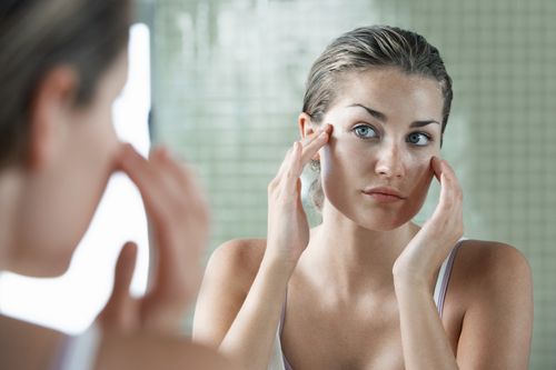 woman looking in mirror touching face