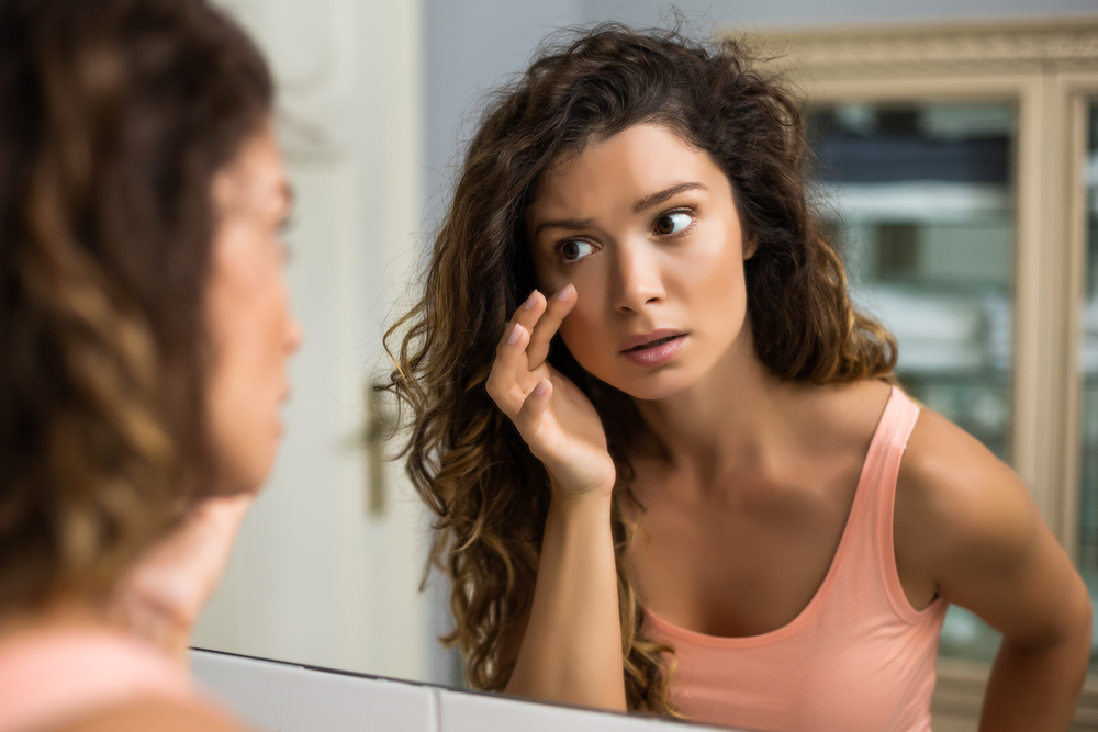 woman touching her face looking in the mirror with concern